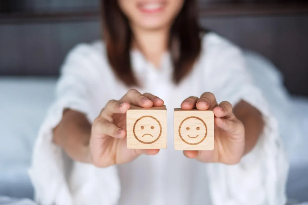 Une personne tenant deux cubes en bois, l'un avec un visage triste, l'autre avec un visage souriant